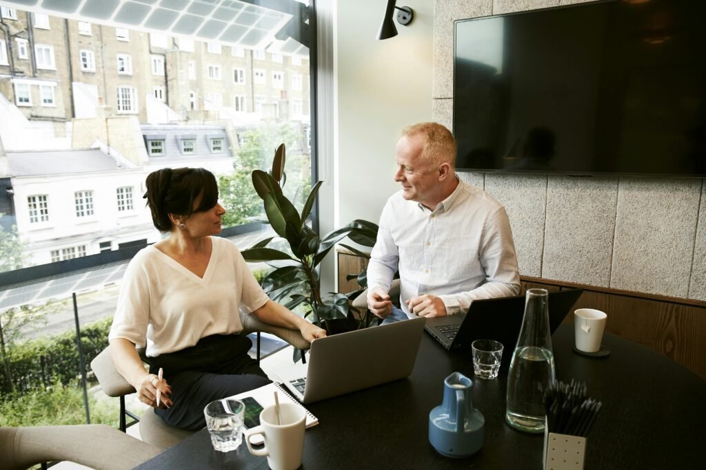pexels-photo-2977565-2977565 Two business professionals engaging in a team meeting in a modern London office with a large window view.